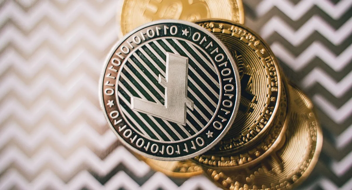 Deux mains tiennent des pièces de crypto sur fond d'écran de trading