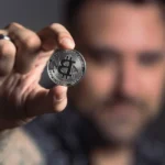 Gros plan sur deux mains tenant une clé USB devant un écran crypto