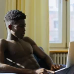 Jeune adulte devant ordinateur cherchant Coflix dans un salon éclairé, air concentré