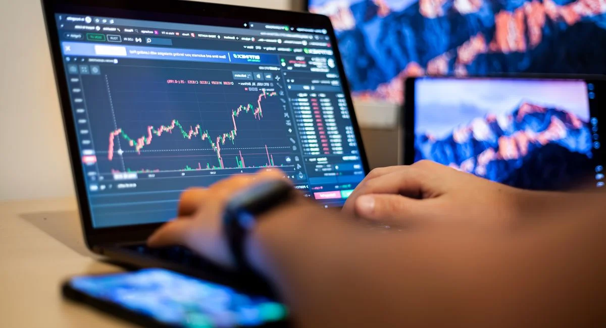 Trois personnes analysent des écrans de trading dans une salle remplie d'ordinateurs