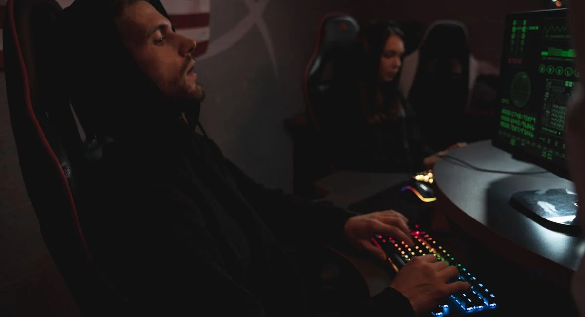 Young adults working on cybersecurity tasks in a dimly lit tech environment.